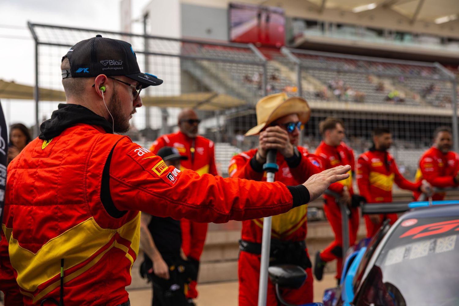 Ferrari racing team members in red uniforms discuss strategy on the pit lane at a motorsport circuit.