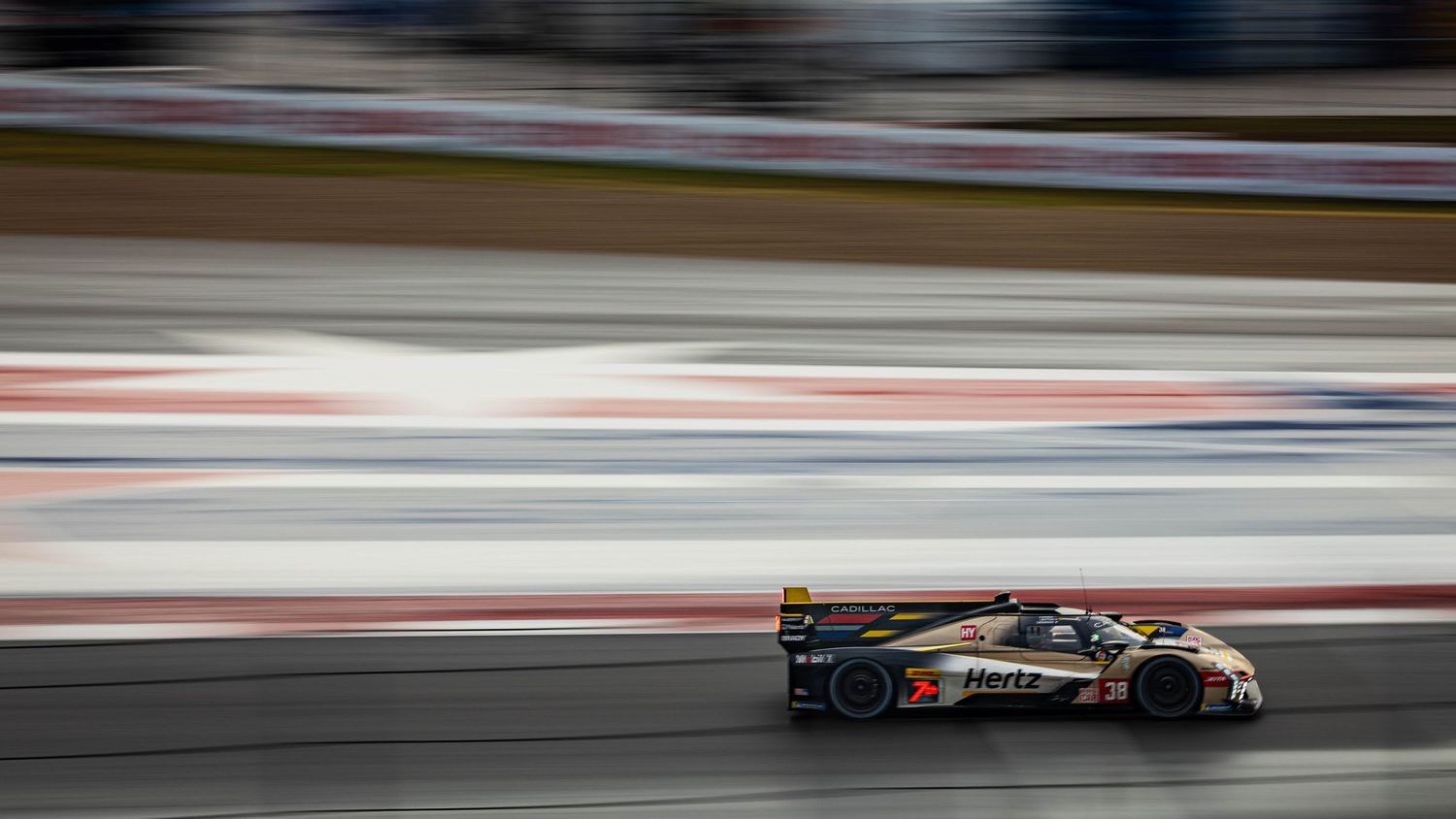 Dark-liveried LMH prototype race car captured with dramatic motion blur speeding along racing circuit.
