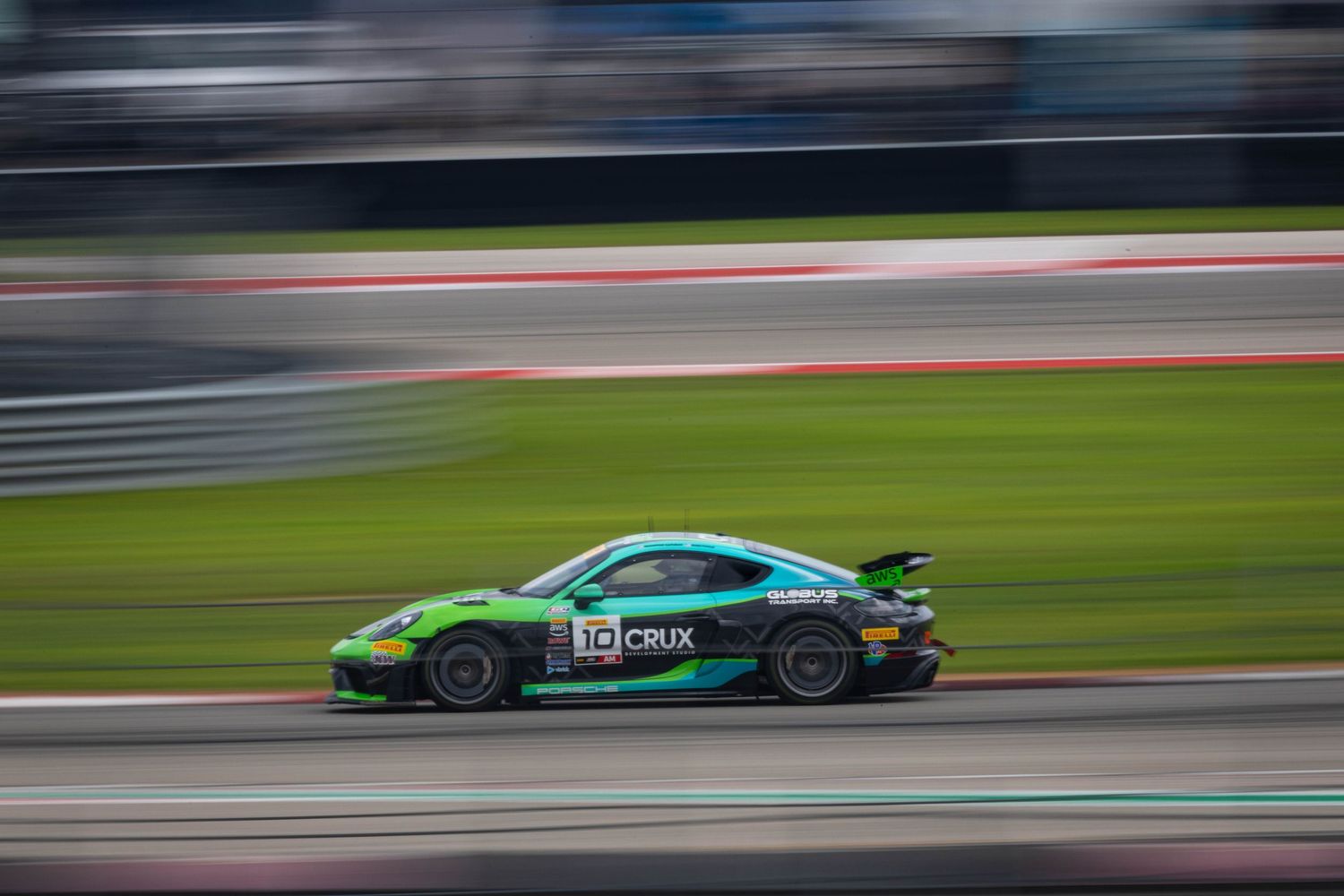 Green Porsche 911 GT3 Cup car racing on a circuit track at high speed.