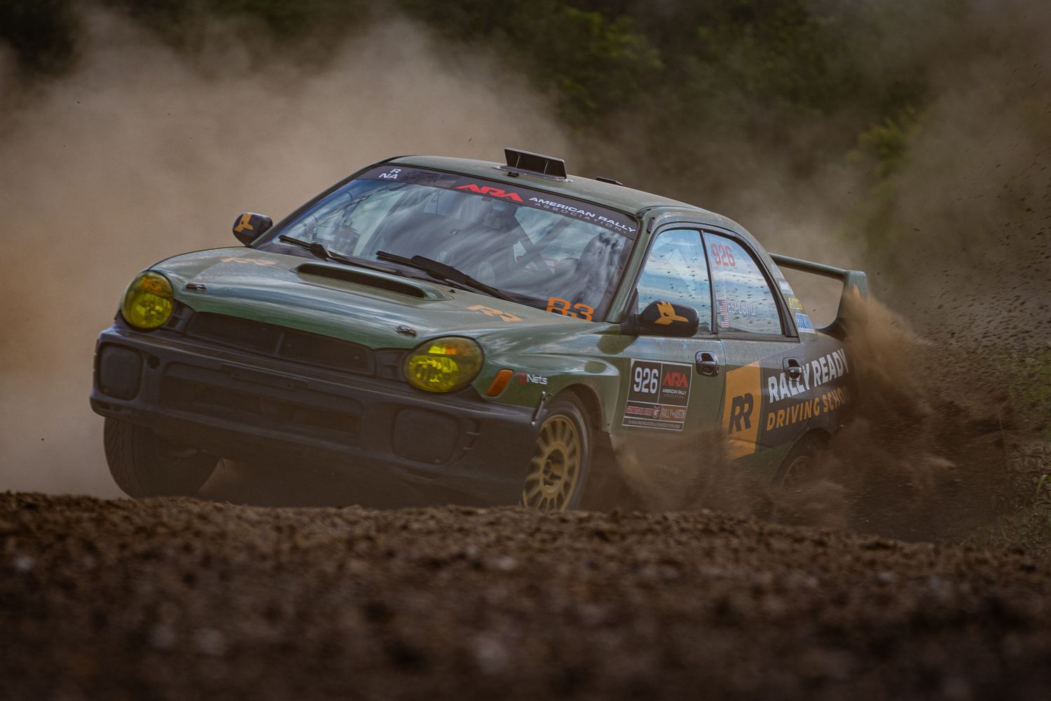 Rally car kicking up dust on a dirt track during an off-road racing competition.