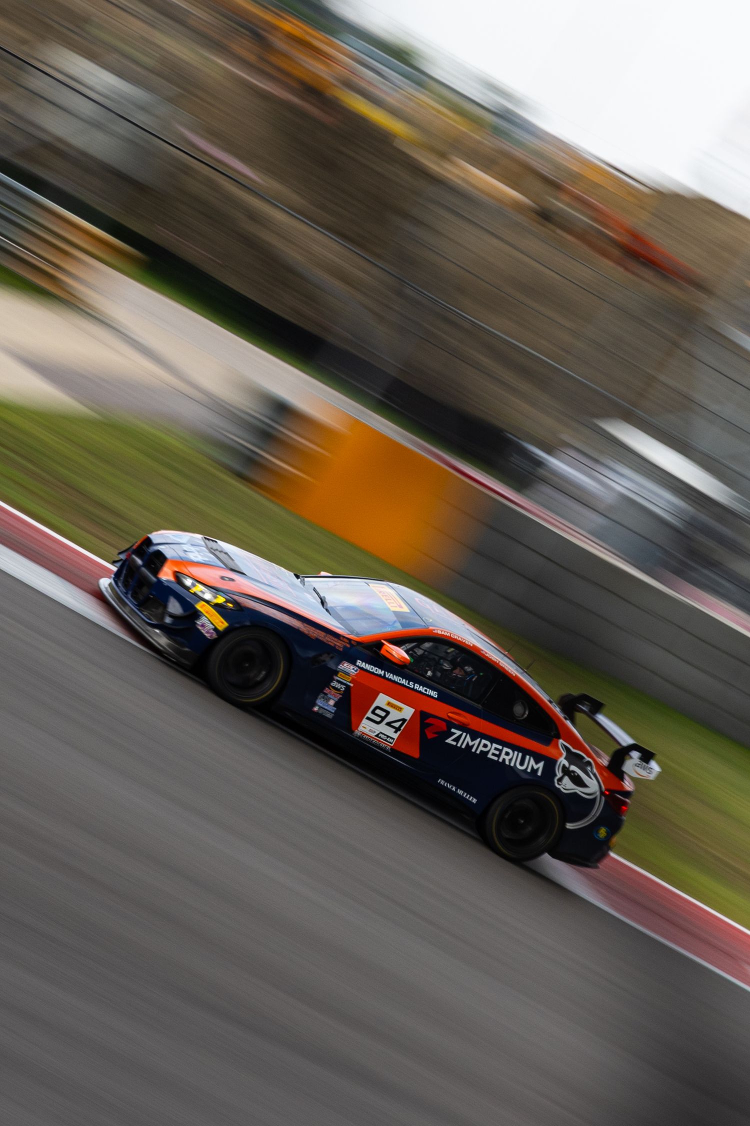 Orange and black Zimperium GT race car number 57 speeding through a motorsport circuit with motion blur.