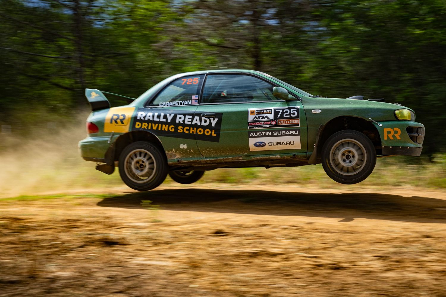 A Rally Ready Driving School Subaru Impreza catches air over a jump on a forest rally stage.