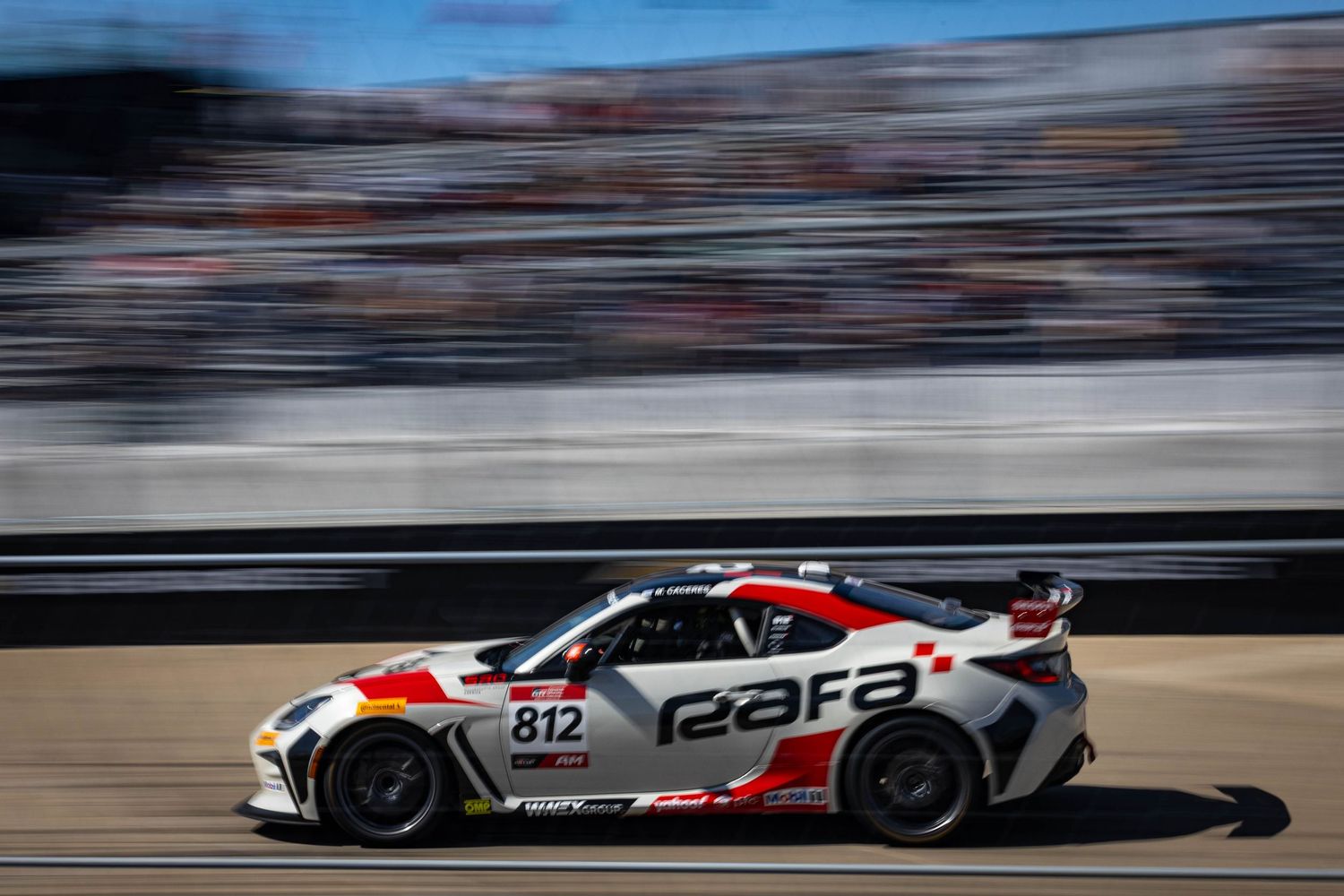 Rafa-sponsored Nissan GT4 race car number 812 speeds along sunlit racing circuit track.