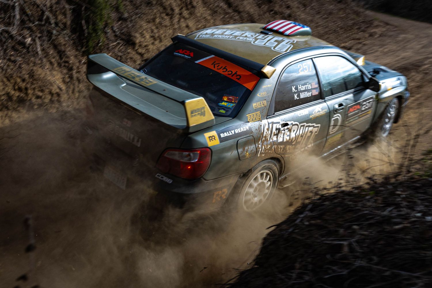 Rally car kicking up dirt and mud on a rugged off-road rally stage competition.