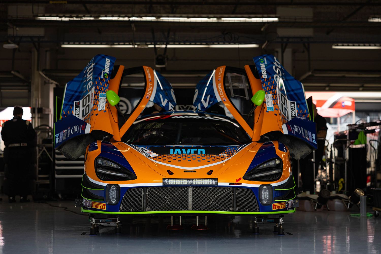McLaren 720S GT3 race car with orange livery parked in pit lane garage.
