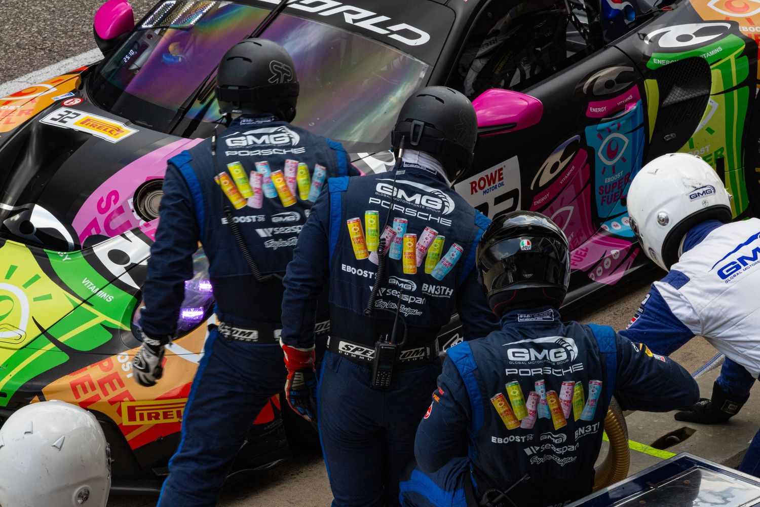 BMG Porsche GT3 pit crew in colorful uniforms performing a pit stop during a race.