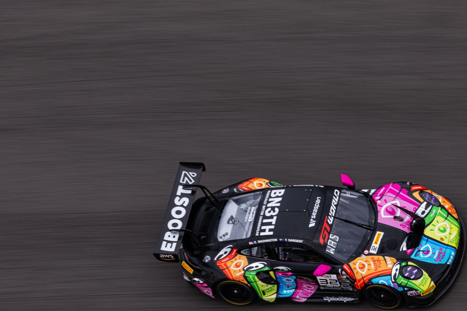 A colorful neon-livery GT3 race car captured in motion blur on a professional racing circuit.