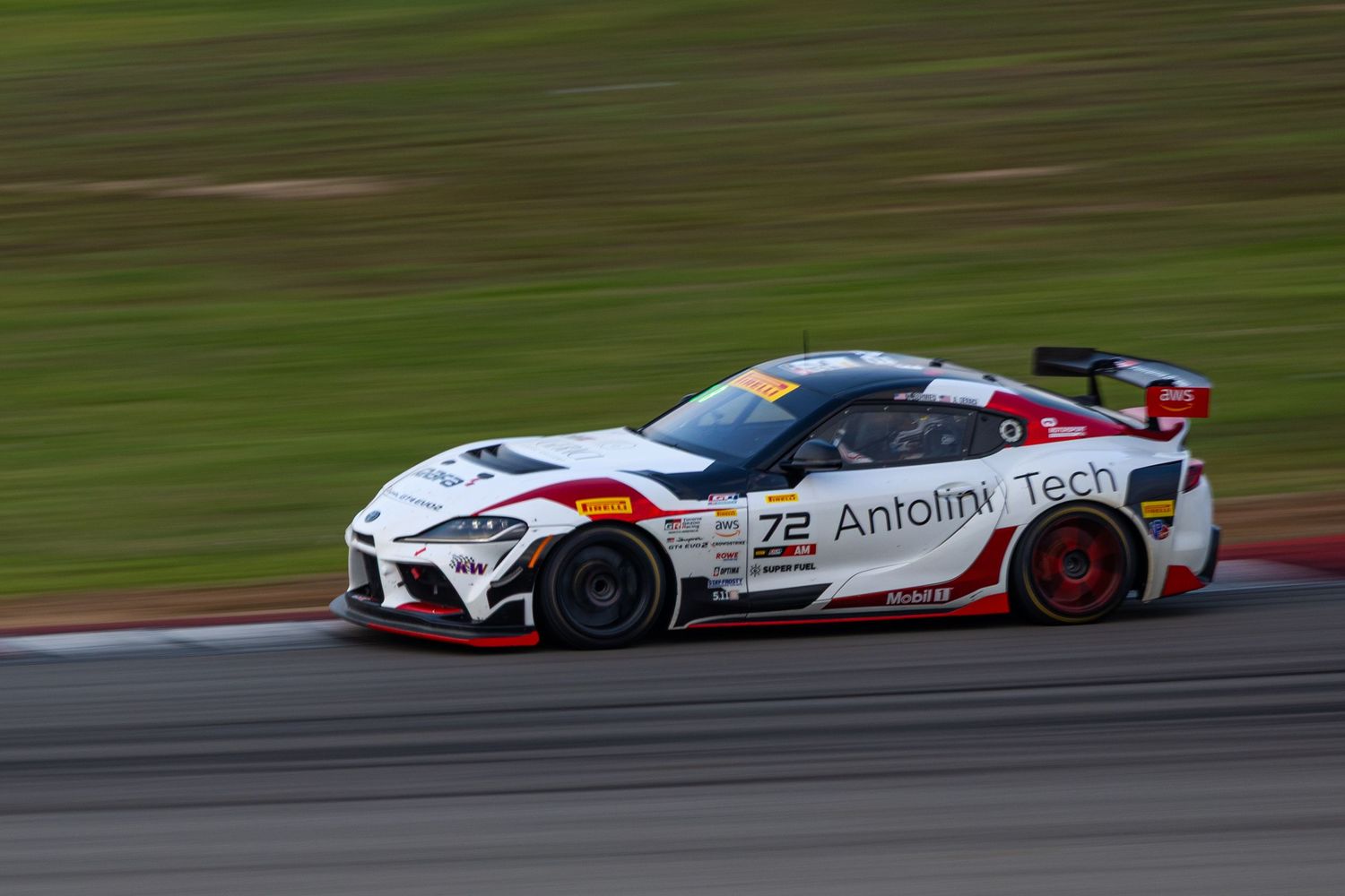 White Toyota GR Supra number 72 with Antolini Tech livery races through a corner at a GT event.