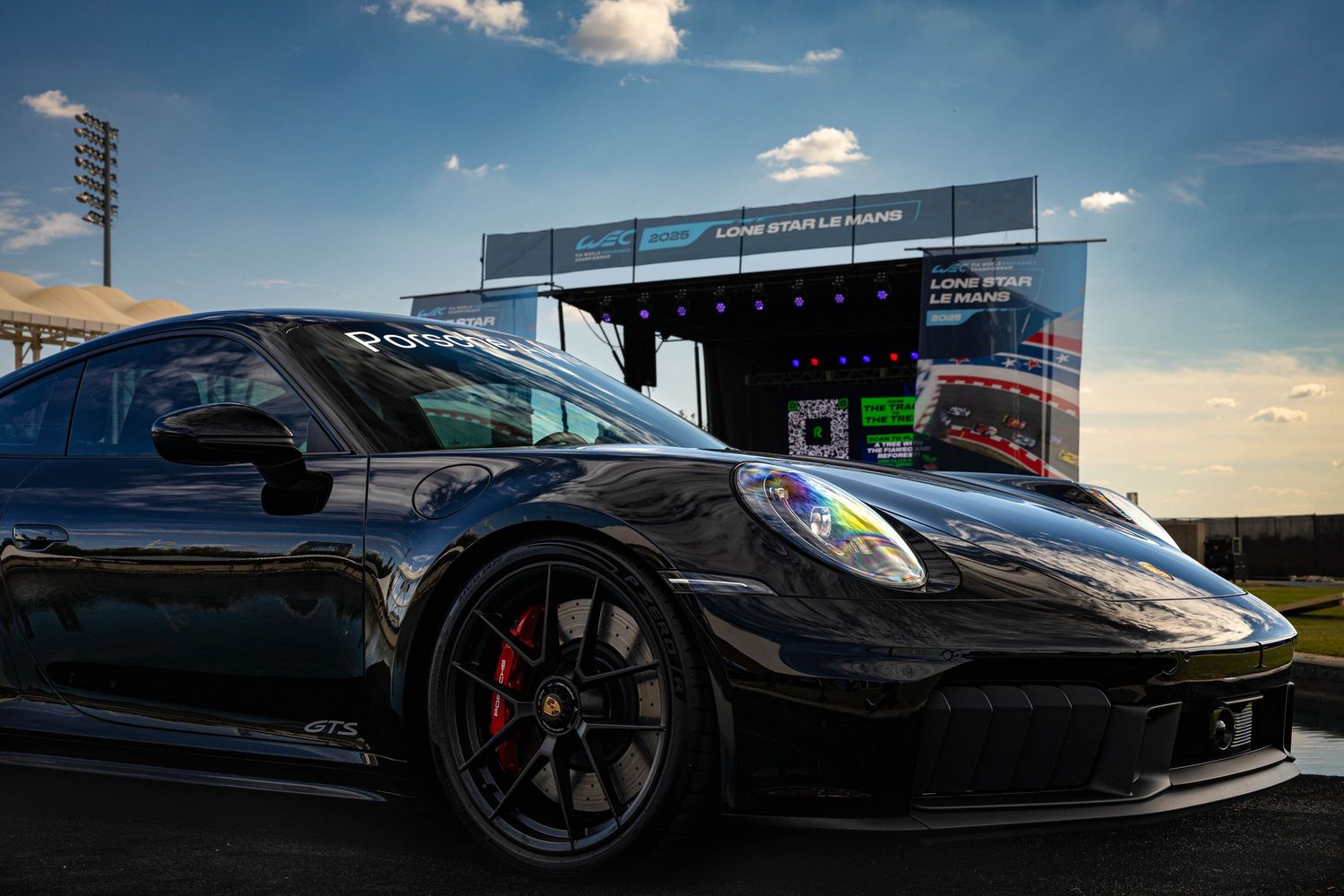 Black Porsche 911 GT3 parked at Lone Star Le Mans racing event under a dramatic sky.