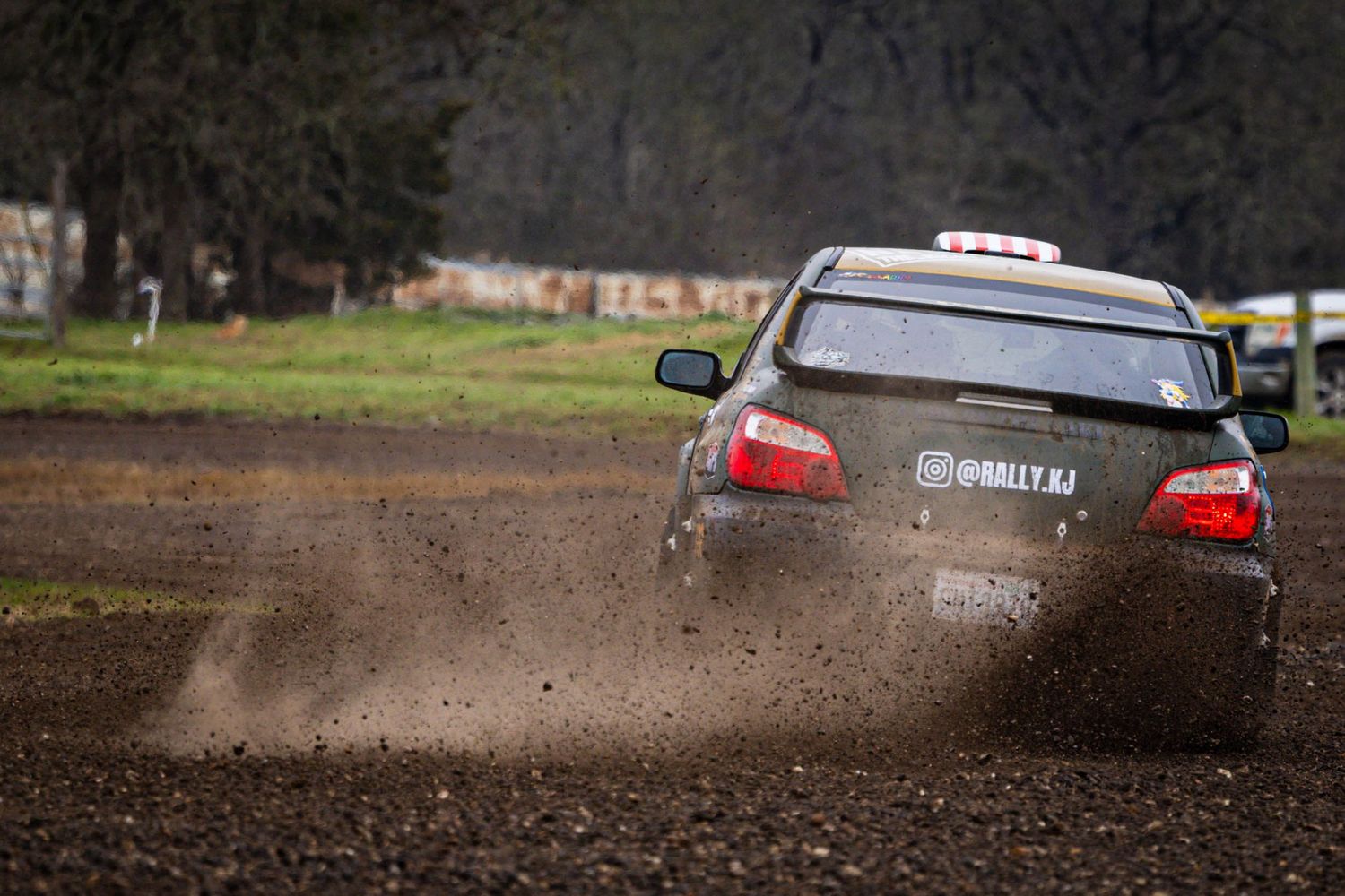 Subaru rally car kicking up dirt and mud on a forest rally stage.