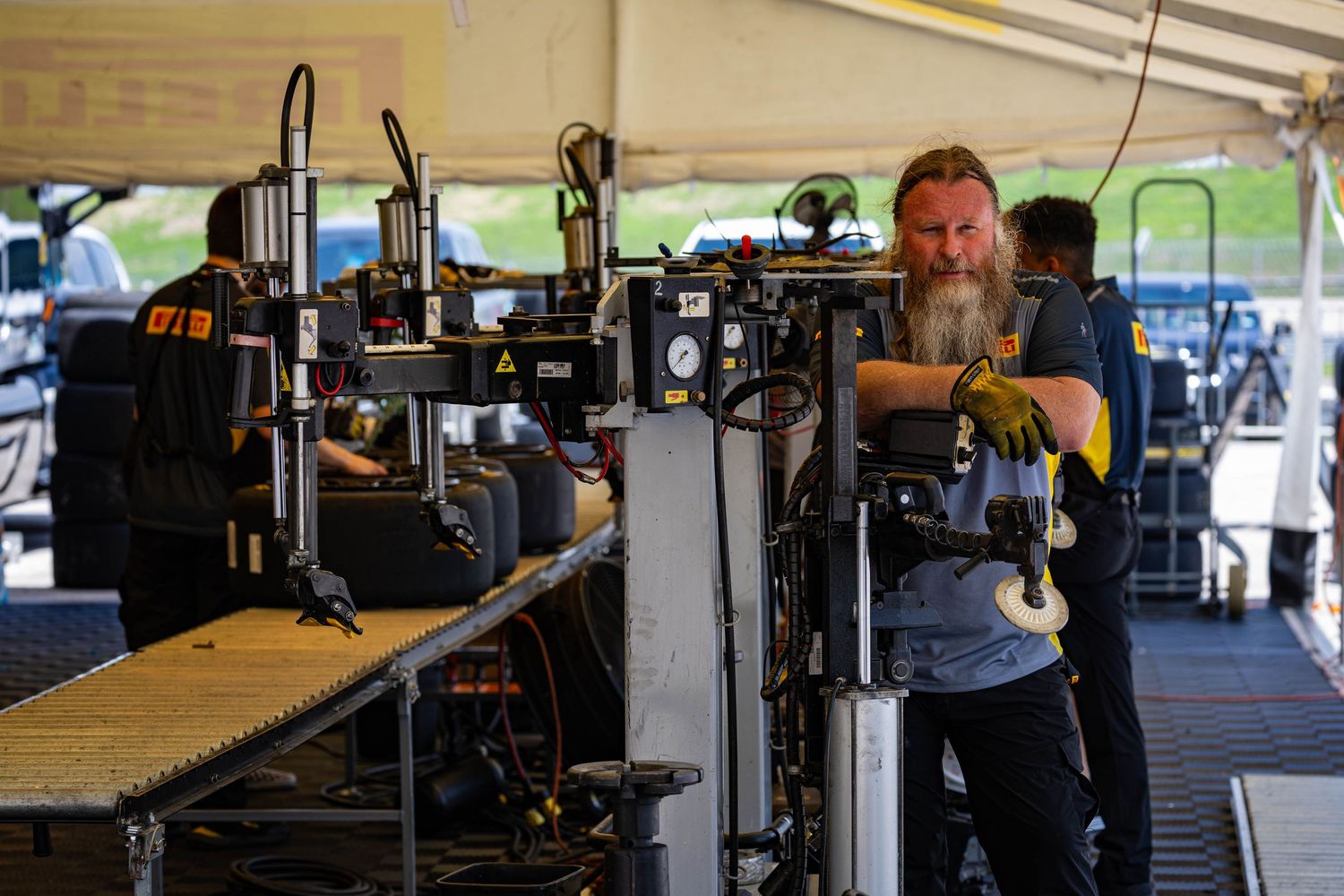 Bearded crew member operating broadcast camera equipment under a tent at a racing event.