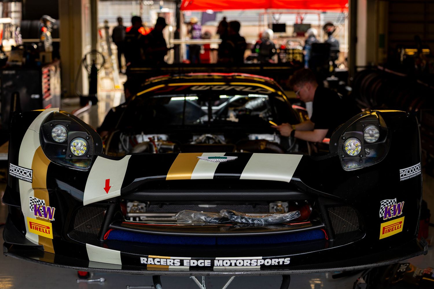 Black and gold Nissan GT-R race car from Racers Edge Motorsports being serviced in pit lane garage.
