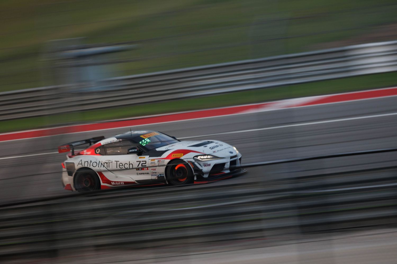 Toyota GR Supra GT racing car speeds along track with dynamic motion blur background.