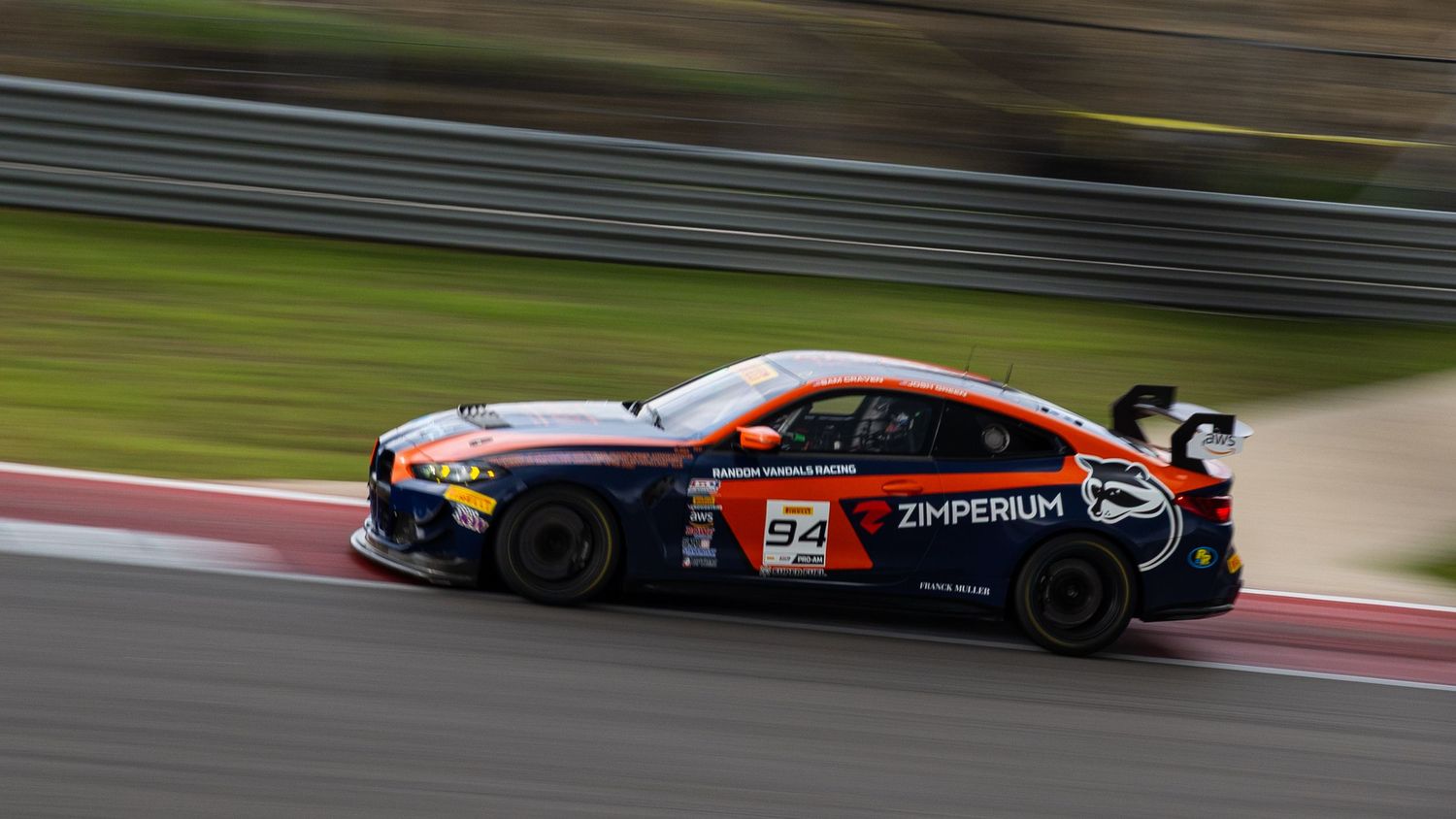 Zimperium sponsored GT race car number 57 in orange and black livery navigating a racing circuit corner.