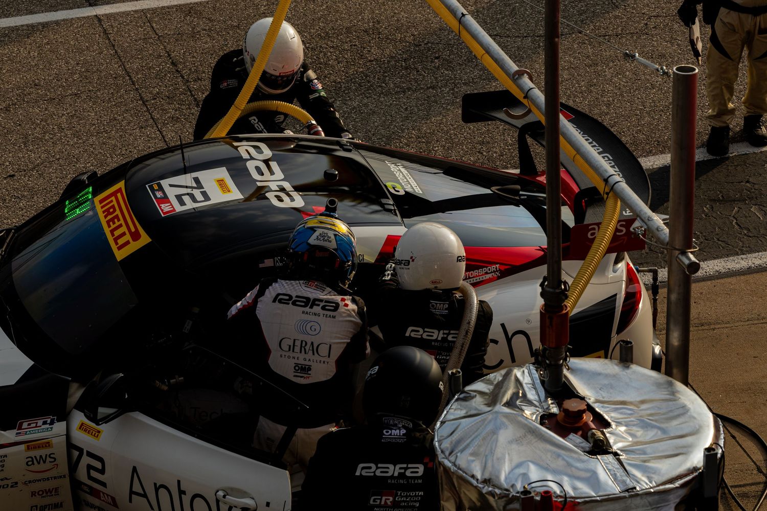 Pit crew members perform rapid tire change on white GT racing car during motorsport competition pitstop.
