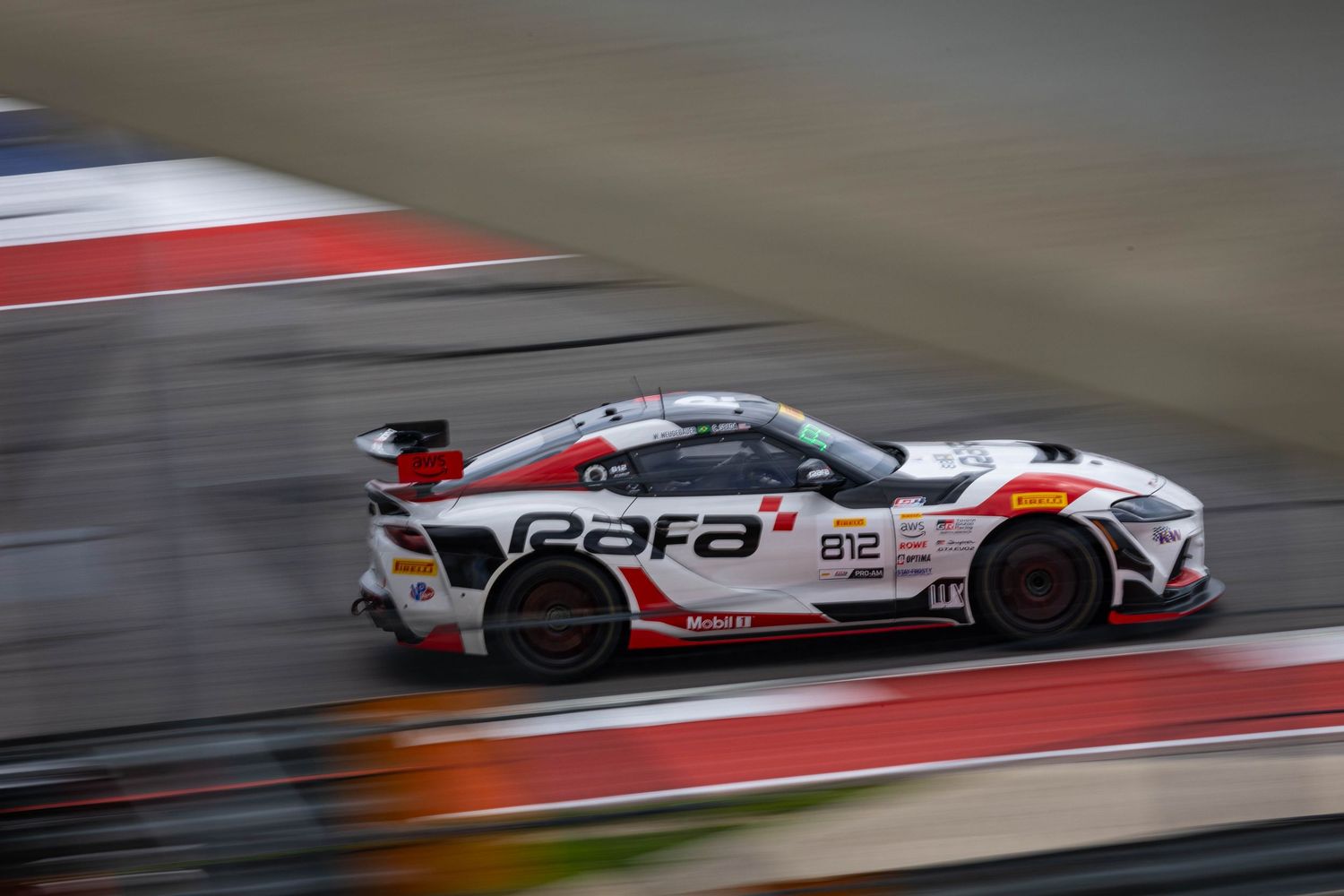 White and red Toyota GR86 GT4 race car speeding on a motorsport circuit.