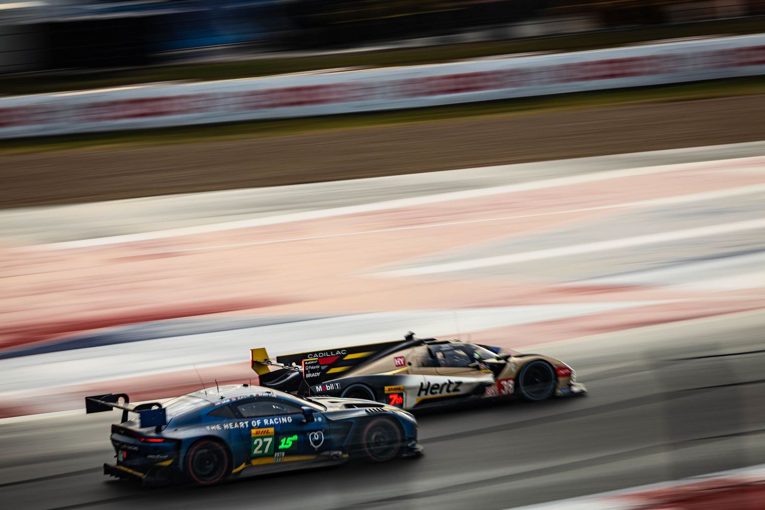 Two GT3 race cars, including Heart of Racing Aston Martin No.27, battling on circuit.