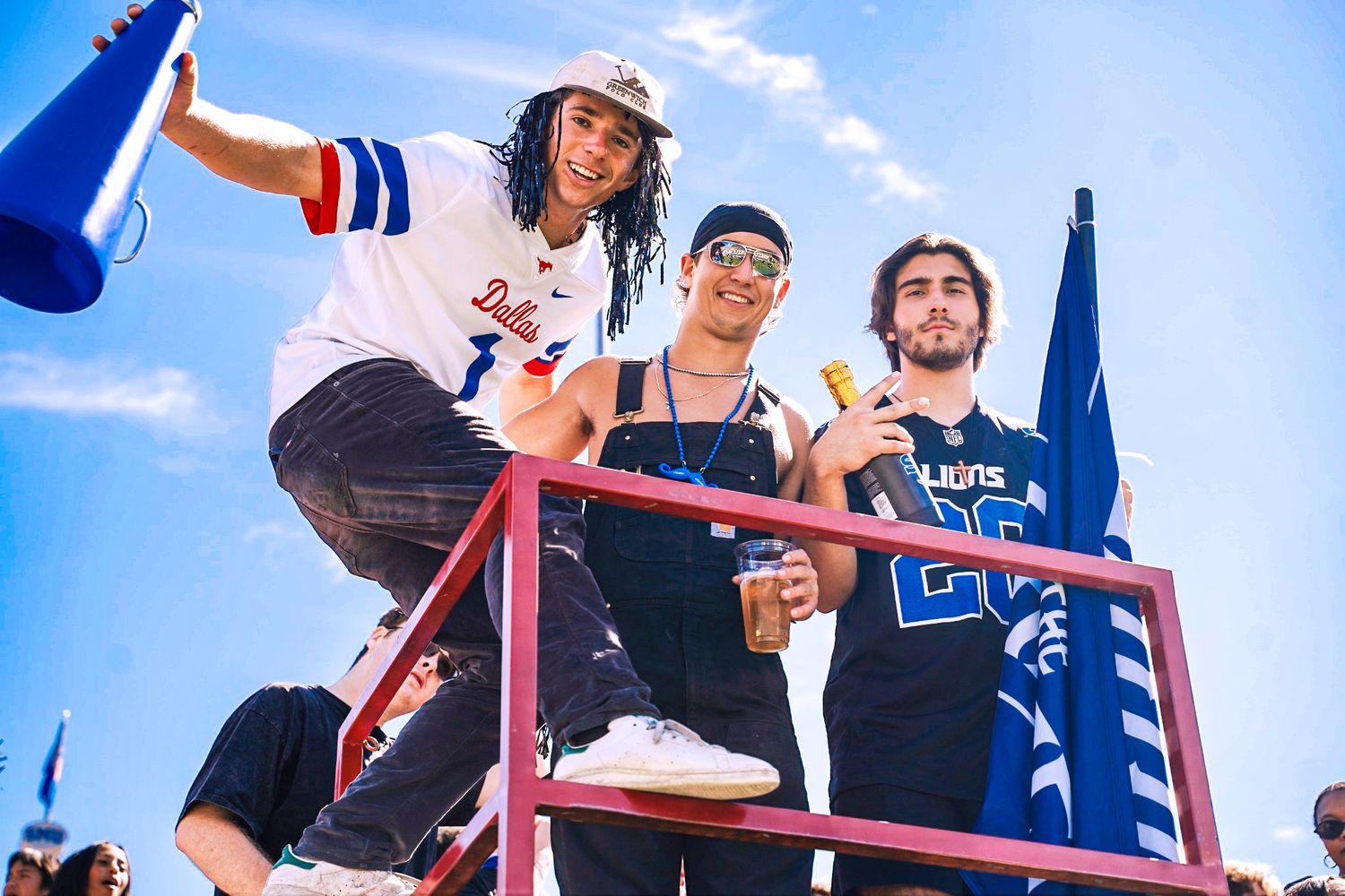 Three energetic college students cheering with megaphone and popsicles at an outdoor university sports event.