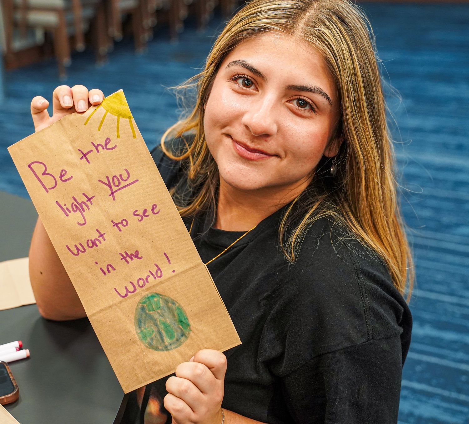 Smiling student holding a brown paper bag with inspirational message Be the light you want to see in the world.