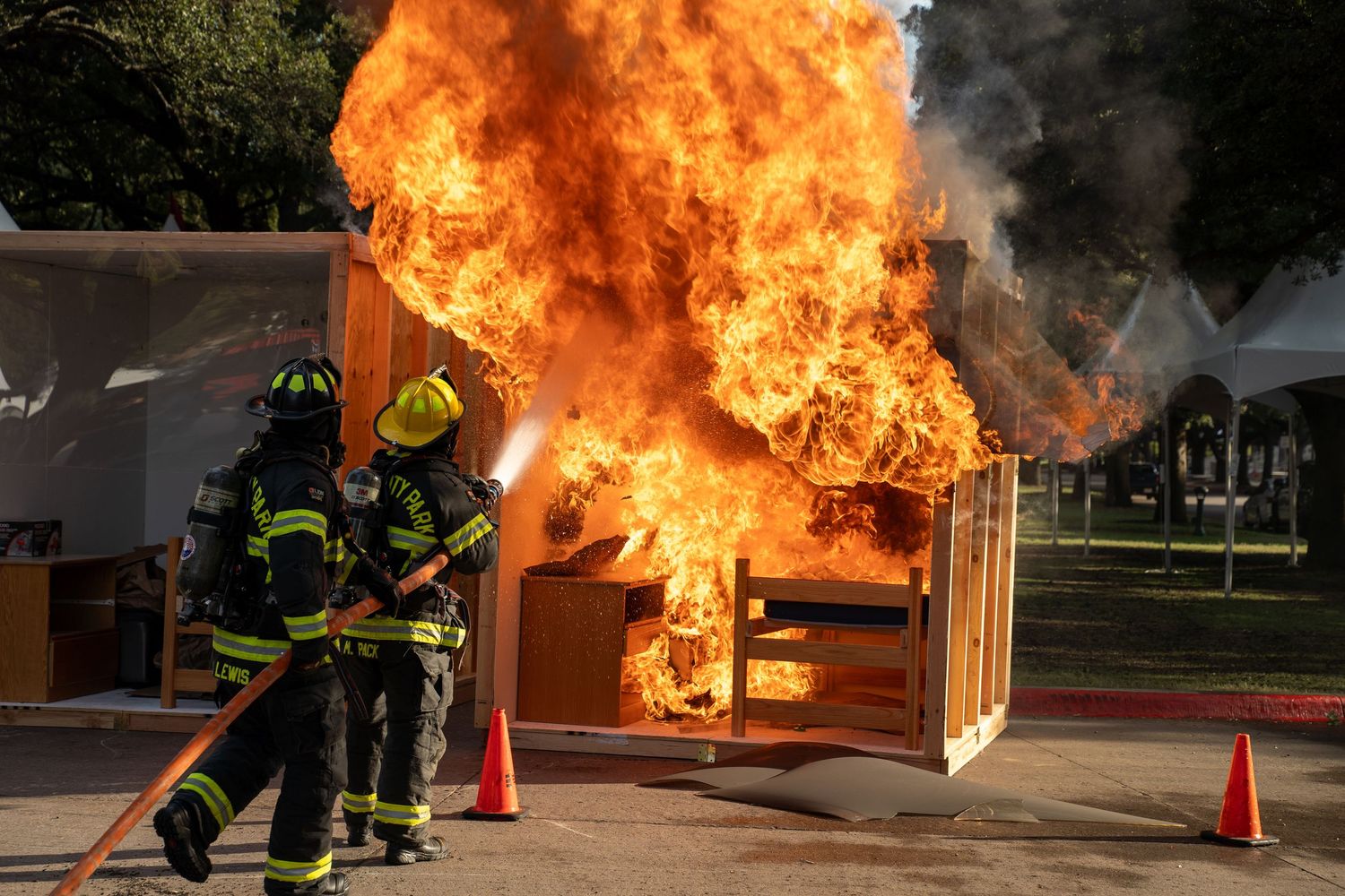 Two firefighters battle a large controlled blaze during an outdoor fire safety demonstration on campus.