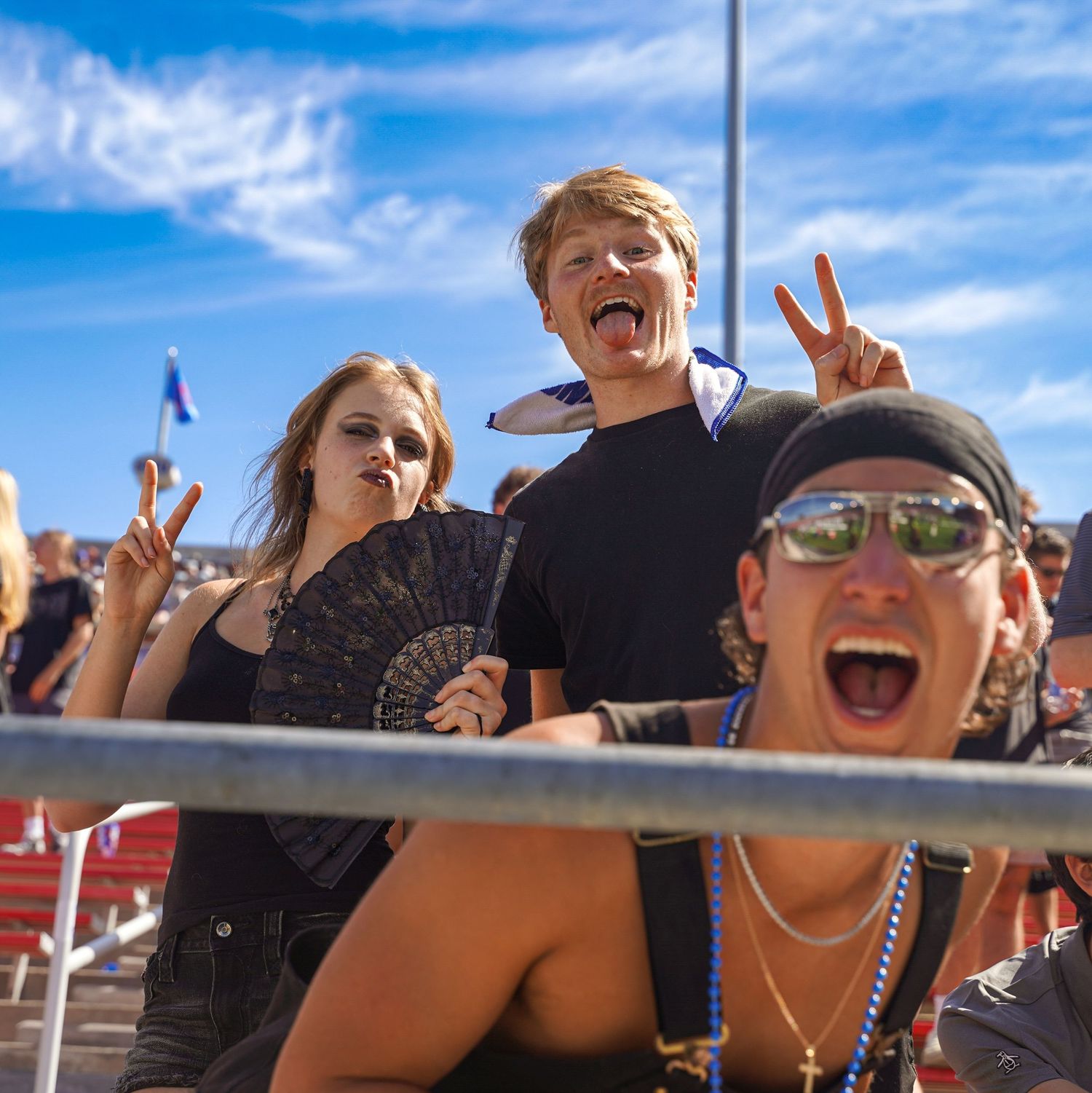 Excited festival crowd making peace signs and funny faces at an outdoor music event on a sunny day.