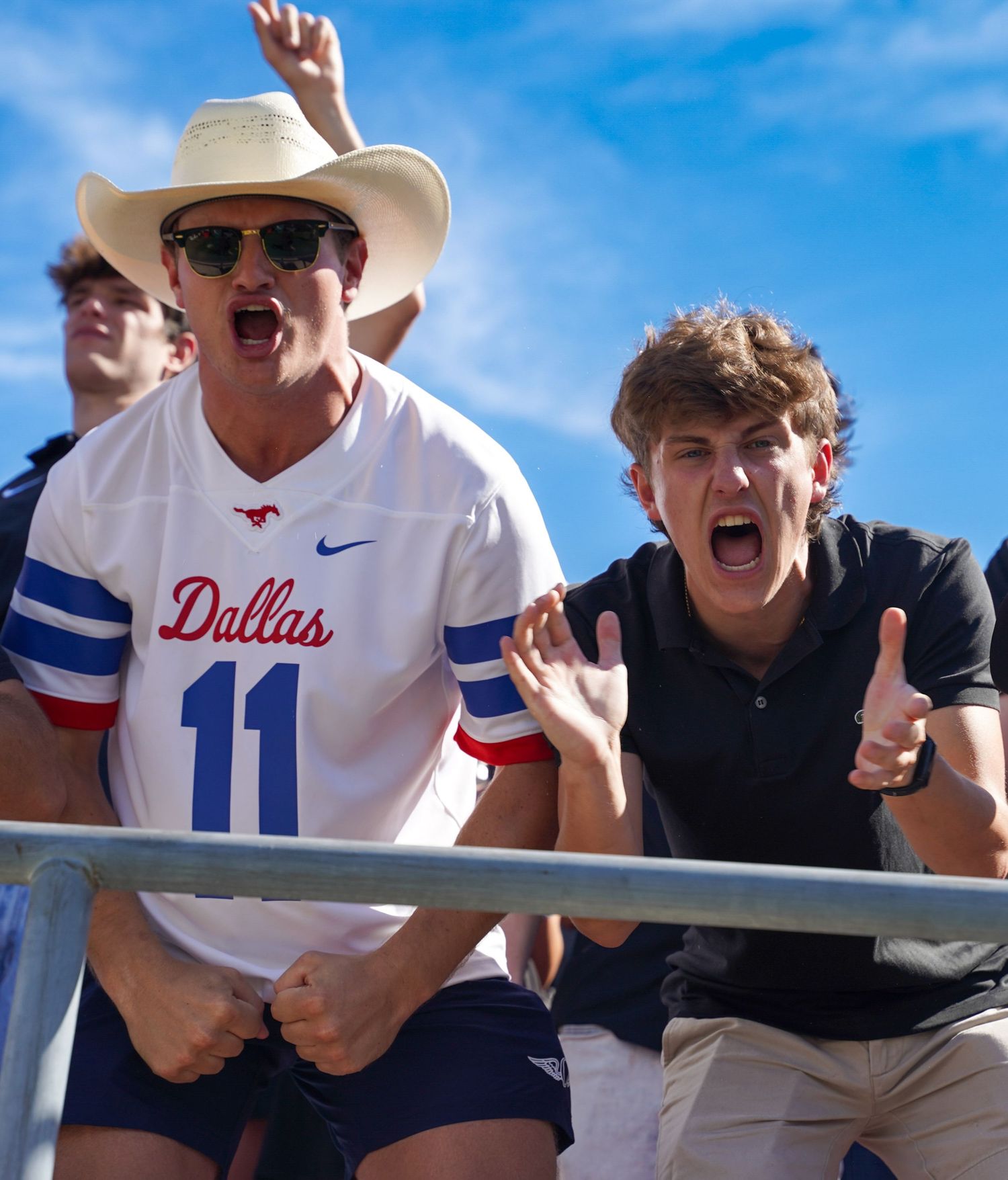 Two enthusiastic fans cheering at a Dallas sports game, one wearing a cowboy hat and Dallas jersey number 11.