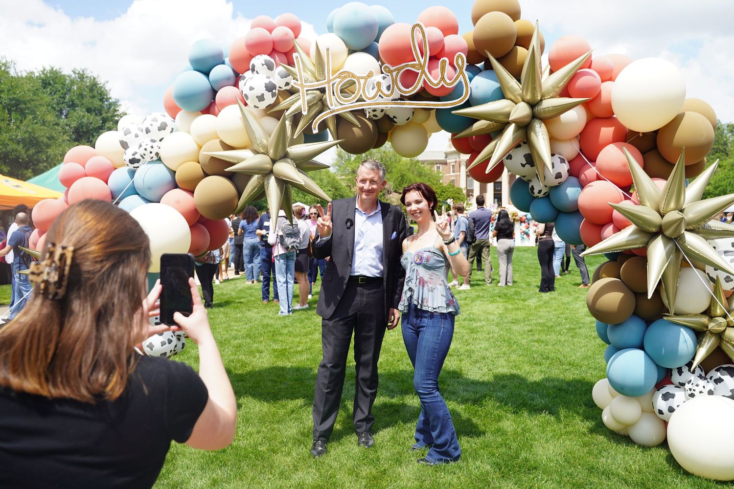 President Hartzell and a Student pose for a photo under a festive balloon arch decorated with star-shaped gold balloons at an outdoor event.