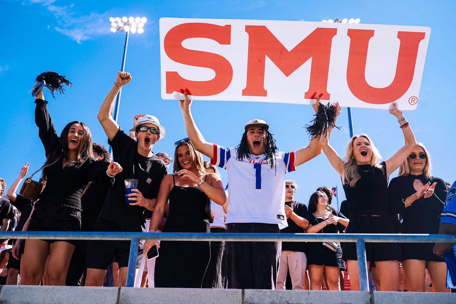 Enthusiastic SMU fans cheering in the stands holding a red SMU sign at a football game.