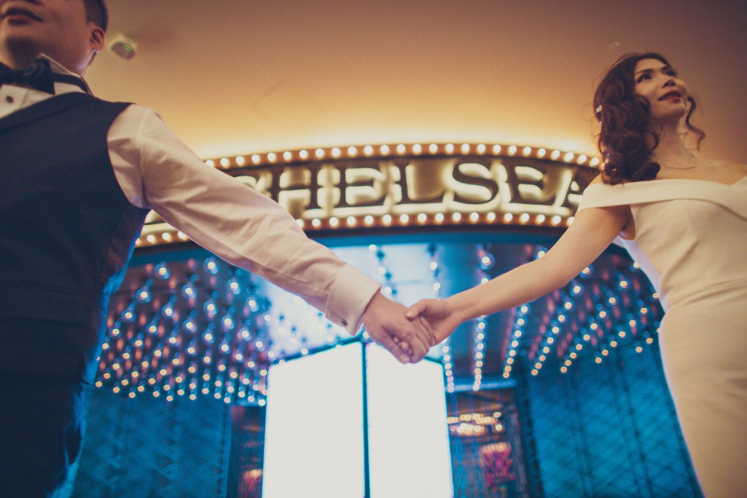 Couple holding hands in front of The Chelsea illuminated marquee sign.