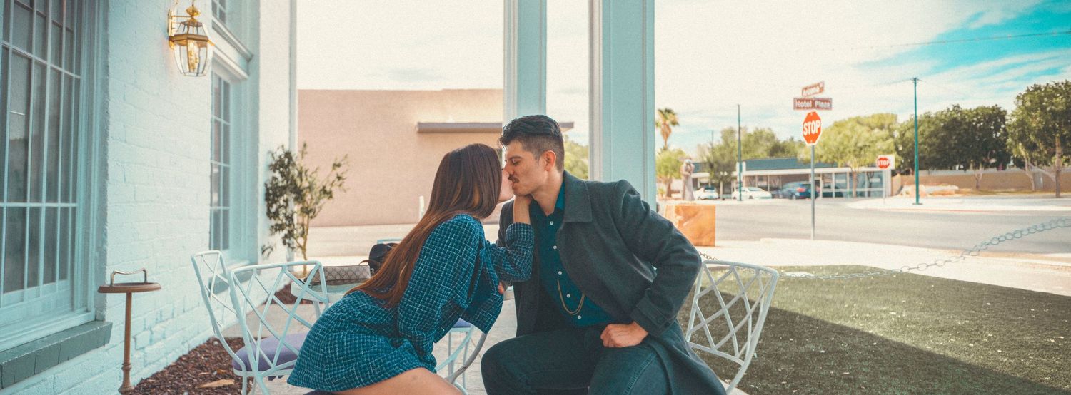 A romantic couple sharing an intimate moment outside a vintage storefront on a sunny day.