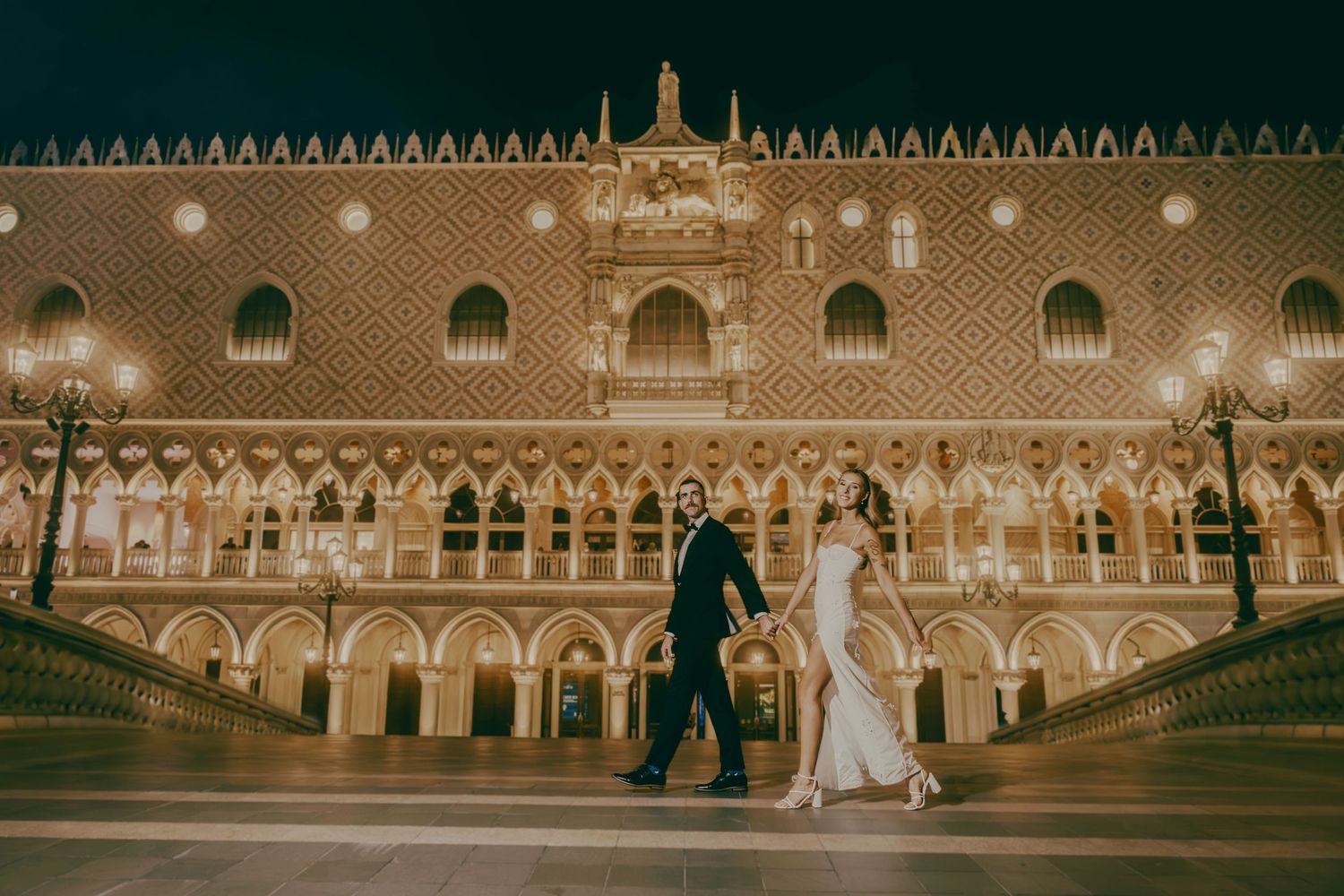 Bride and groom walking hand in hand in front of The Venetian Las Vegas at night.