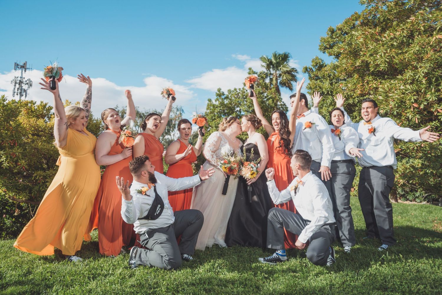 Wedding party celebrating outdoors with bridesmaids in orange dresses and groomsmen in white shirts.