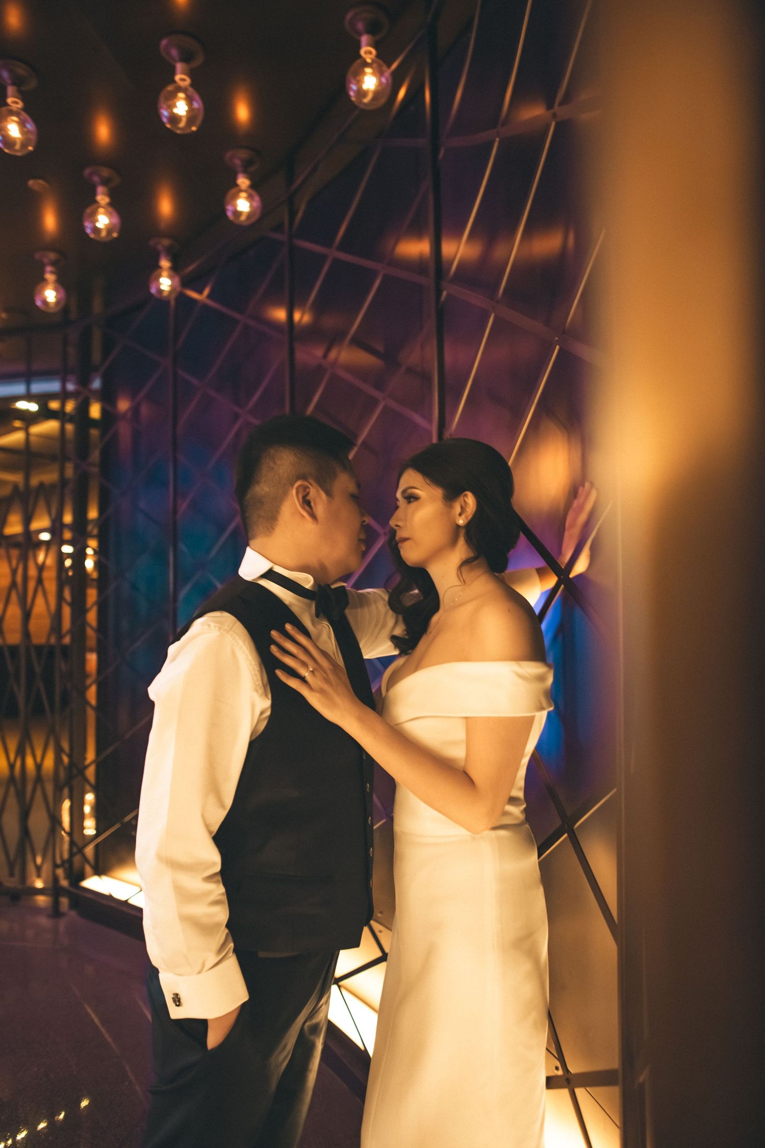 Bride and groom sharing intimate moment in warmly lit venue with geometric golden decor backdrop.