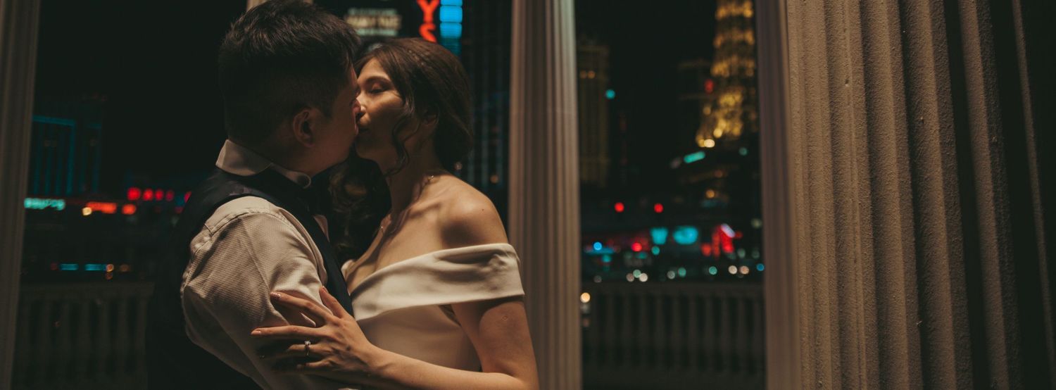 Romantic couple sharing an intimate moment by a window with a glowing city skyline at night.