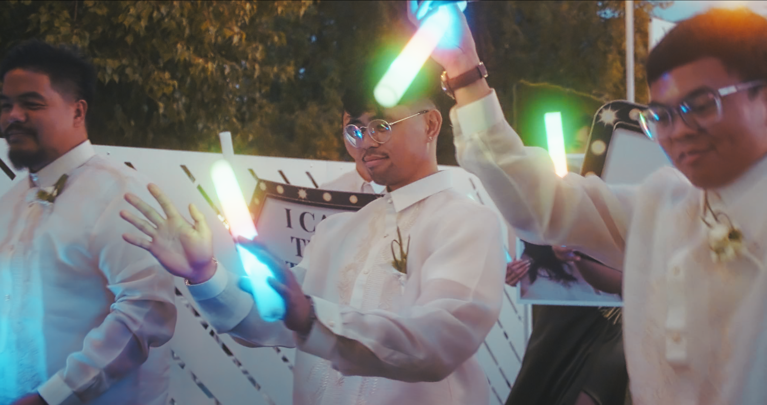 Men in barong tagalog holding colorful glow sticks at wedding celebration.
