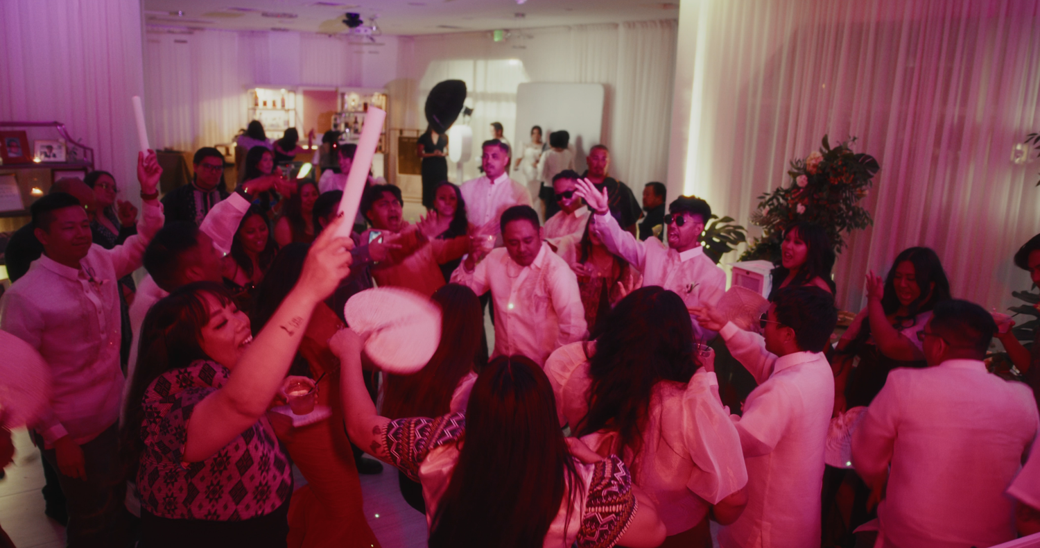Energetic wedding reception dance floor filled with guests celebrating under pink lights.