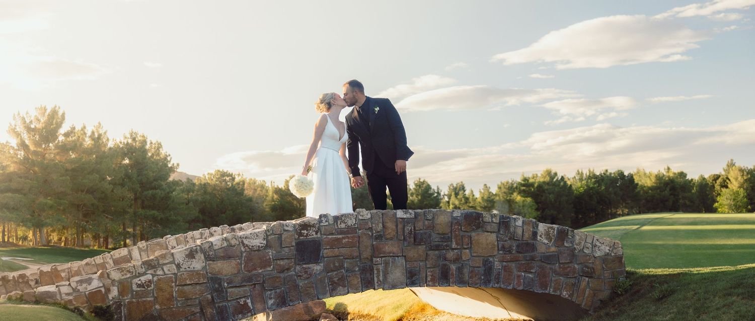 Bride and groom kissing on stone bridge at golden hour outdoor wedding.