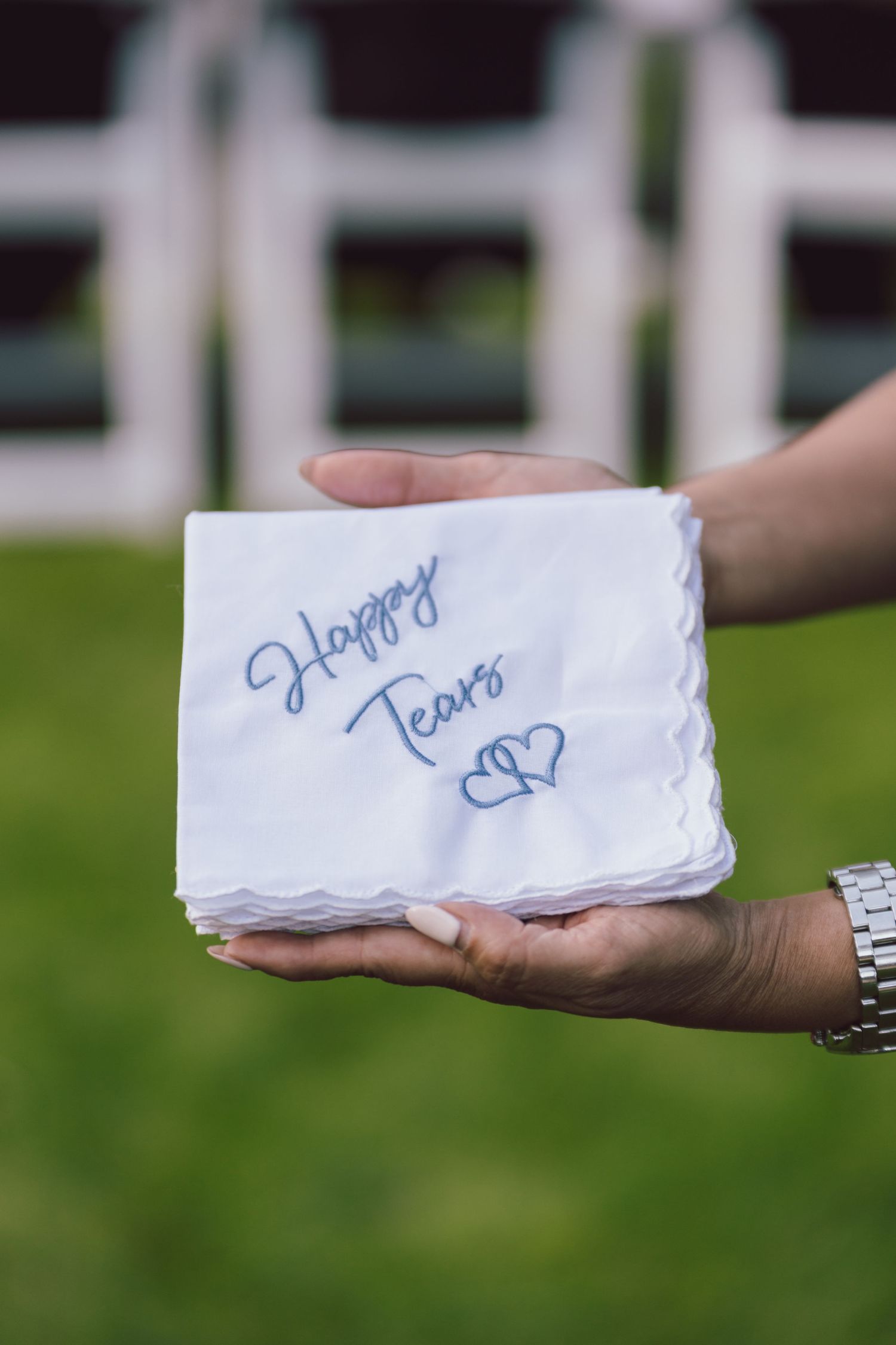 Hands holding white embroidered handkerchief reading Happy Tears at wedding.