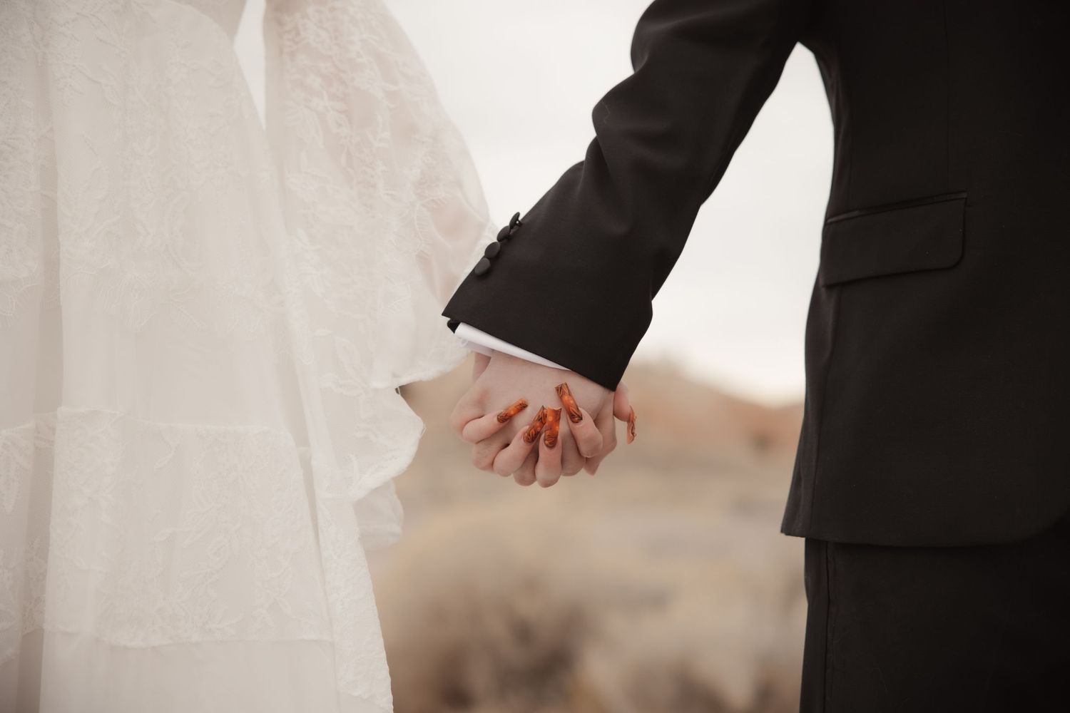 Close-up of bride and groom holding hands, bride in white lace dress and groom in black suit.