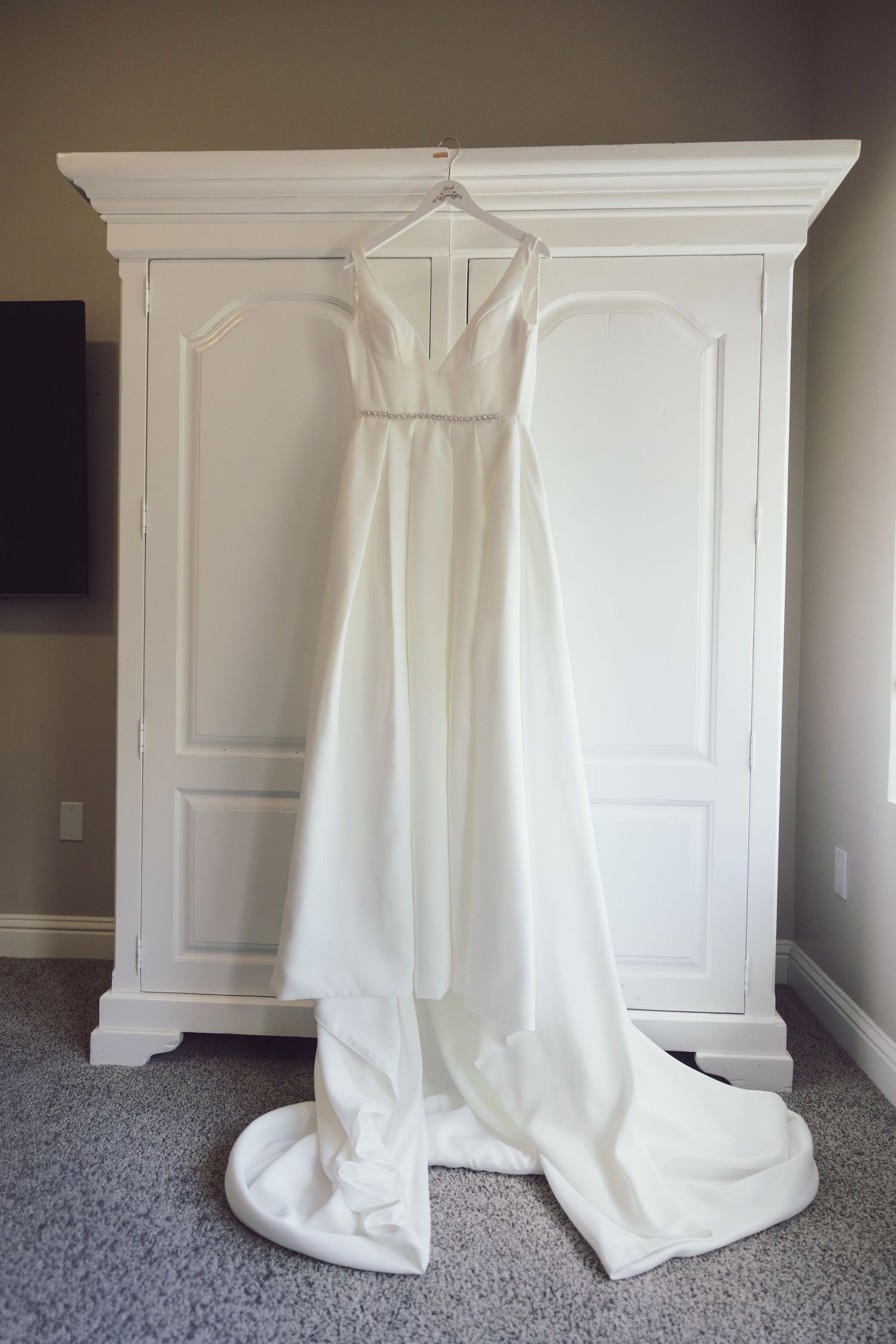 Elegant white A-line wedding dress with train hanging on white armoire.