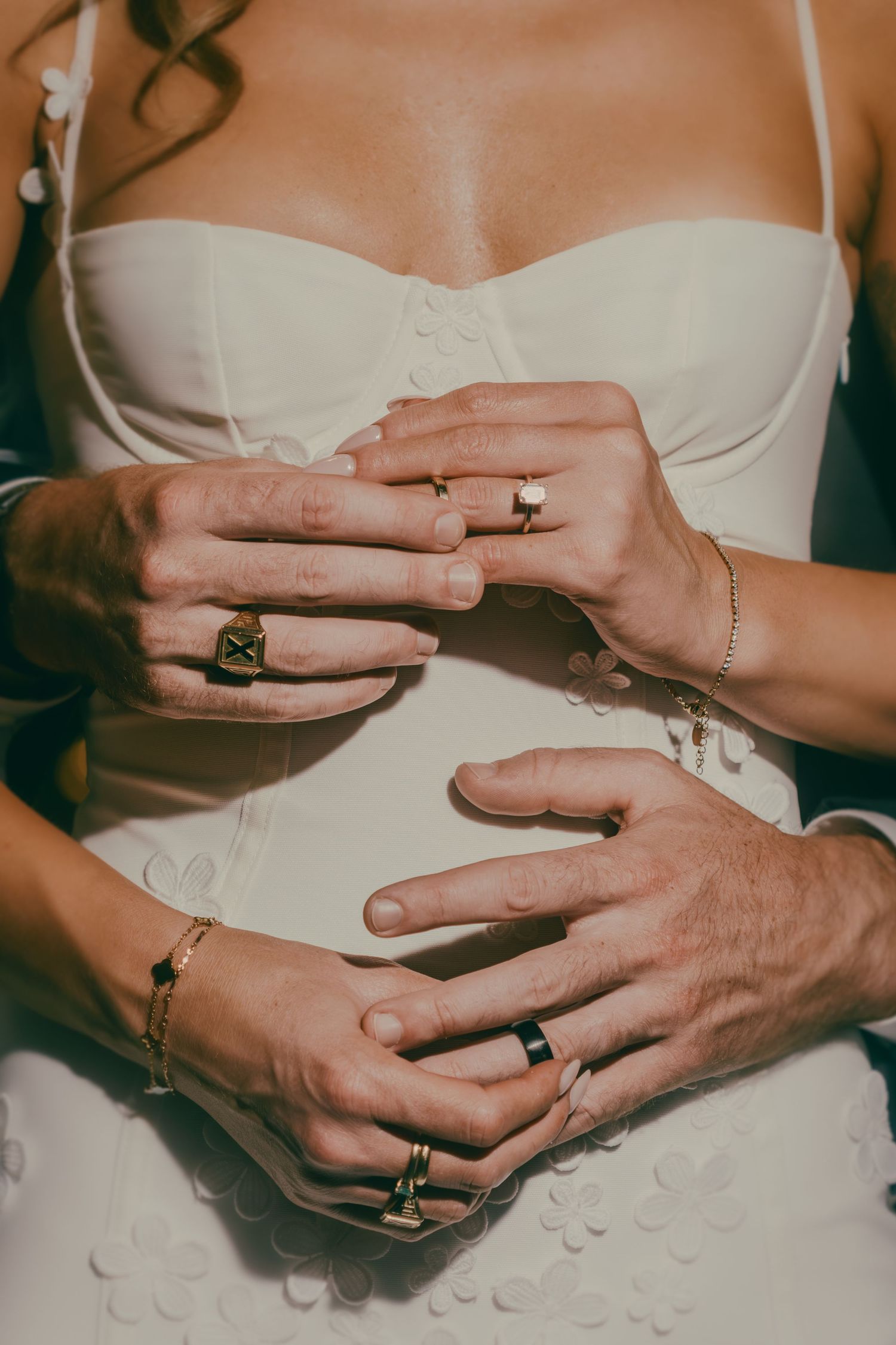 Close-up of bride and grooms hands showing wedding rings and jewelry on brides white dress.