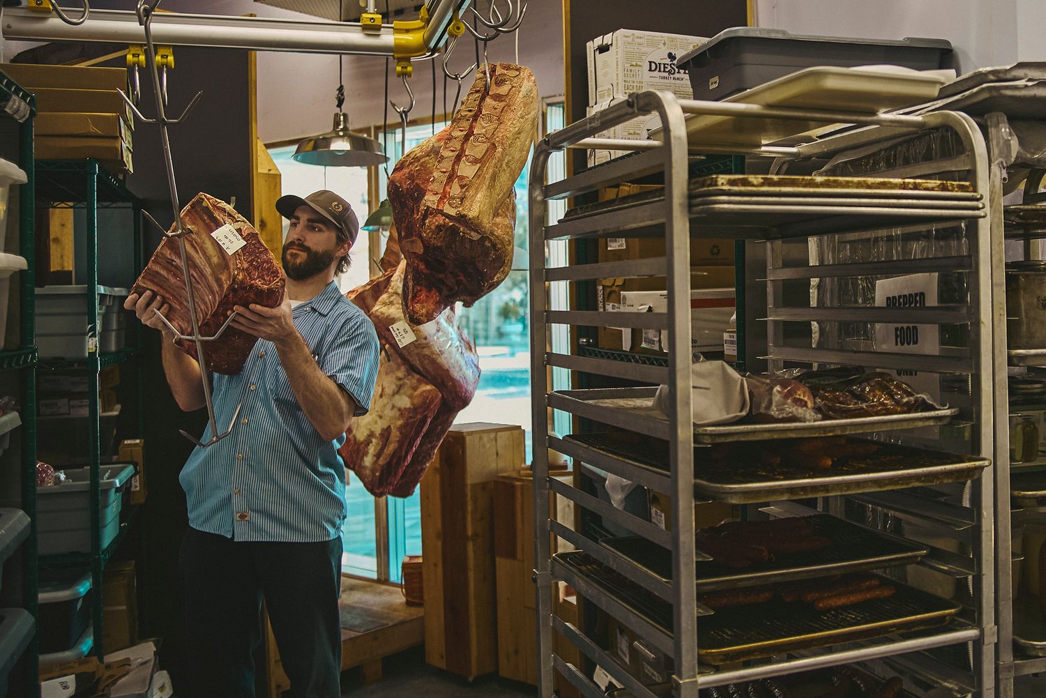 Baker holding freshly baked artisan bread loaves in a professional bakery with metal rack shelving.
