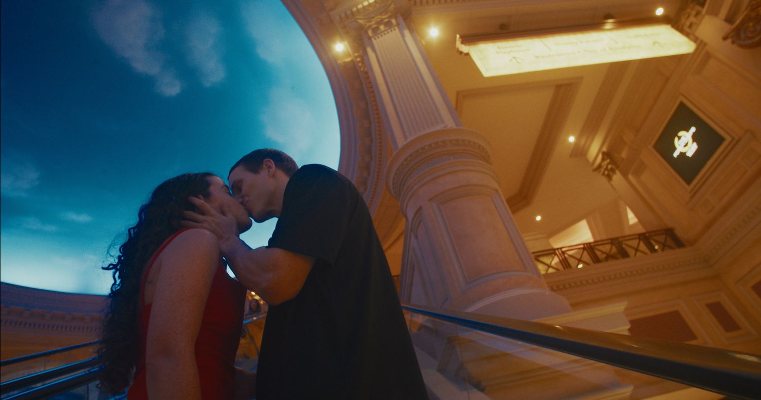 Couple sharing a romantic kiss inside an ornate luxury hotel lobby with grand architecture.