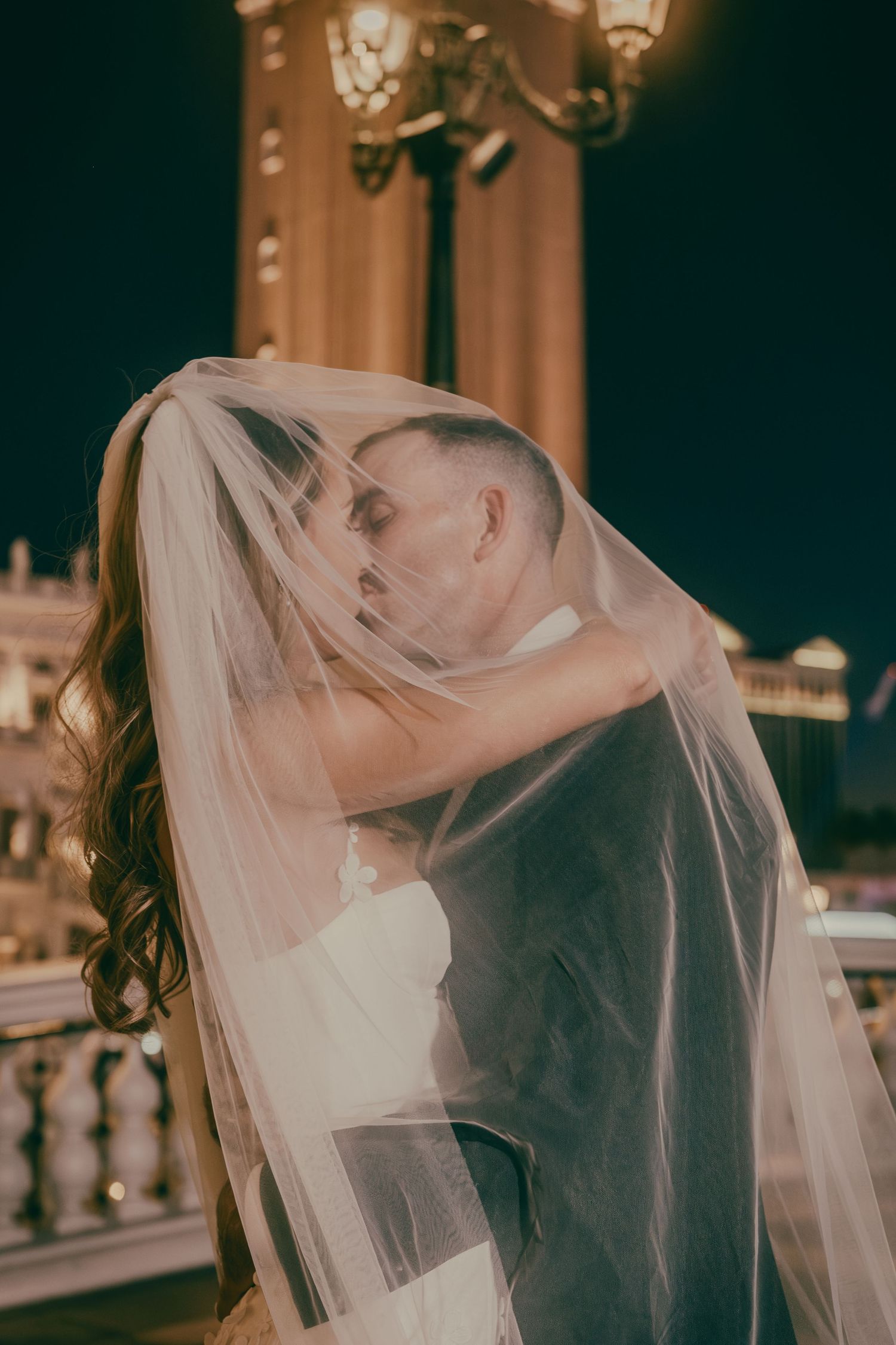 Bride and groom sharing a kiss hidden beneath the brides flowing veil at night in Las Vegas.