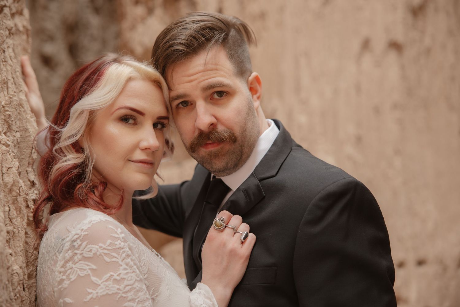 Intimate wedding portrait of bride and groom leaning close together against a textured stone wall.