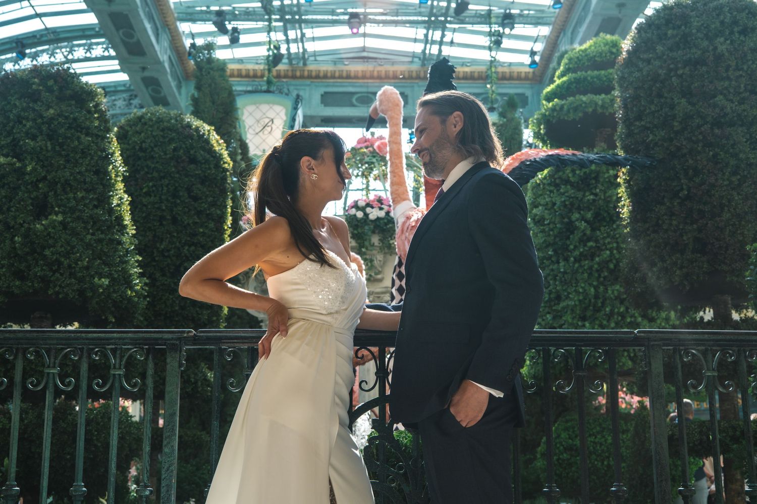 Bride and groom share a romantic moment on a balcony surrounded by lush topiary at Bellagio.