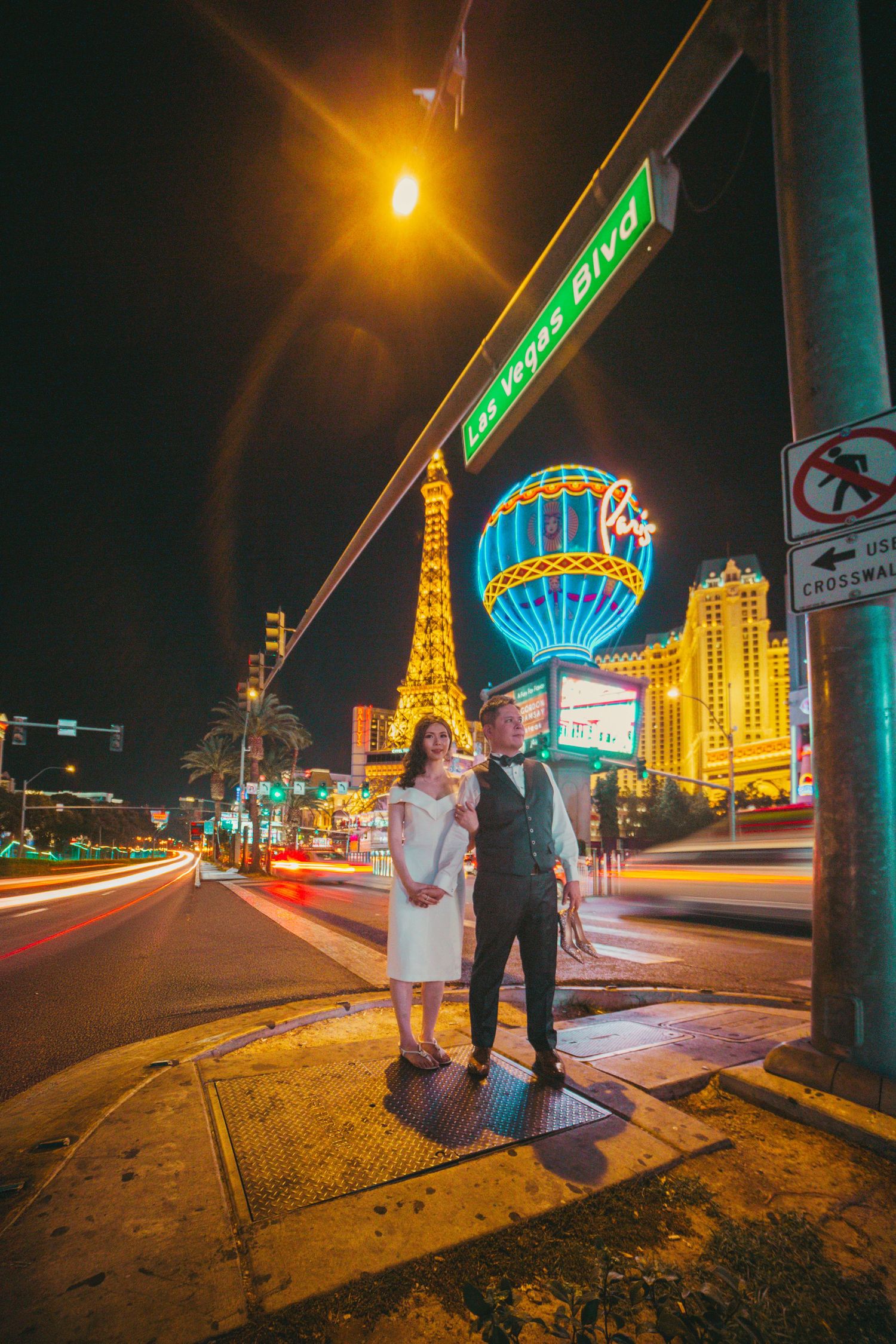 Wedding couple posing on Las Vegas Blvd at night with Paris Hotel Eiffel Tower replica glowing behind them.