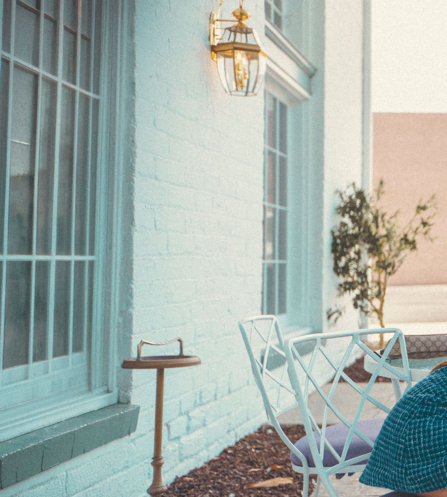 Charming light blue brick porch with gold lantern, white chairs, and small side table in warm afternoon light.