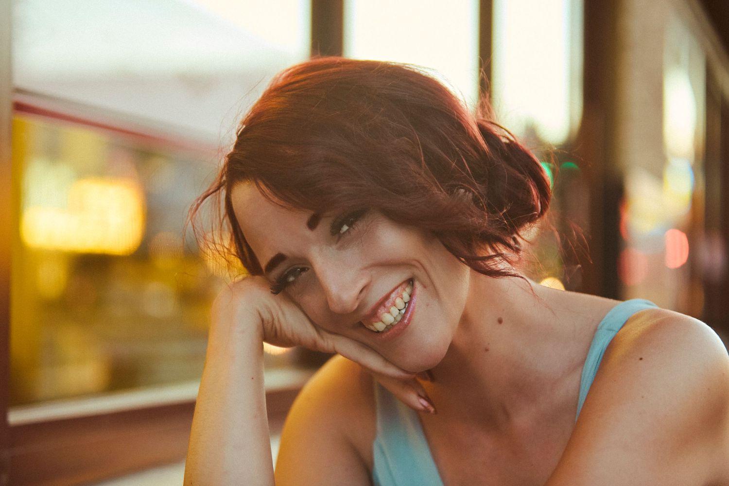 Smiling brunette woman resting her chin on her hand at an outdoor cafe during golden hour sunset.