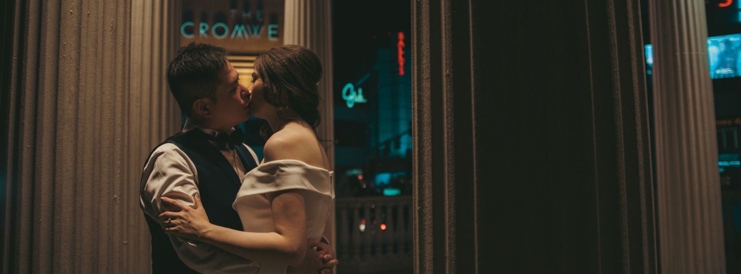 Couple sharing a romantic kiss outside a glowing Cromwell sign at night in an intimate urban setting.